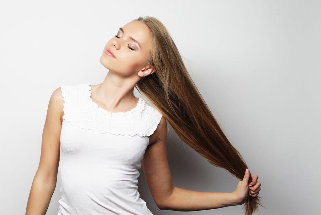 Moça segurando seu cabelo comprido, forte e hidratado, mostrando o fortalecimento capilar. 