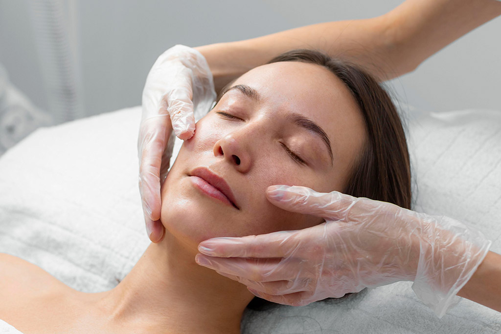 Maos sobre o rosto de uma mulher aplicando skincare